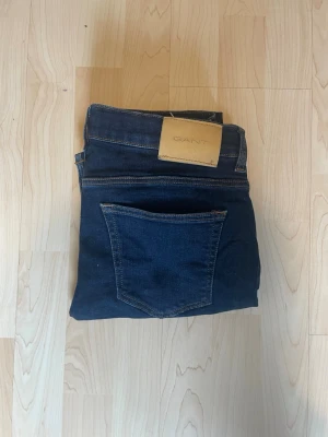 Mörkblå skinny jeans från Gant - Snygga mörkblå skinny jeans från Gant med klassisk femficksdesign och läderpatch med logga bak i midjan. Jeansen har smal passform och är tillverkade i ett stretchigt denimtyg som sitter bekvämt hela dagen med storlek 164.