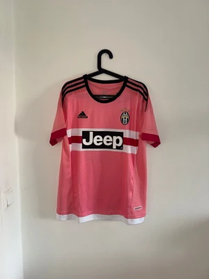 Juventus rosa matchtröja Pogba #10 - Juventus rosa matchtröja från Adidas med Pogba och nummer 10 på ryggen. Tröjan har svarta och vita detaljer, Jeep-logga på bröstet och klubbmärke. Tillverkad i lätt och ventilerande material, perfekt för fotboll eller träning.