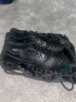 Svarta Nike Tiempo fotbollsskor - Säljer ett par svarta Nike Tiempo fotbollsskor med klassisk låg profil och snörning. Skorna har en stilren design med diskret Nike-logga på sidan och är tillverkade i syntetmaterial och läder för bra bollkontroll. Perfekta för dig som vill ha grym touch på planen. Skorna är elite! Pris kan diskuteras och om du har frågor är de bara att ställa dom!
