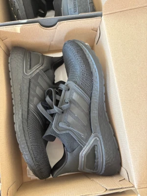 Svarta Adidas Ultraboost sneakers - Snygga helsvarta Adidas Ultraboost sneakers med stickad ovandel och klassiska tre ränder på sidan. Skorna har en chunky sula i Boost-material för extra komfort och en modern, sportig look. Perfekta för dig som gillar stilrena och bekväma sneakers.