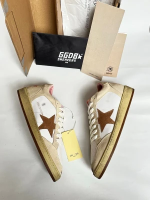 Golden Goose vita sneakers med stjärna - Golden Goose sneakers i vitt skinn med beige mockadetaljer och brun stjärna på sidan. Skorna har vita snören, perforerad tå och rosa detaljer på häl och plös. Sula i beige och brunt. Klassisk låg modell med retrovibbar och GGDB-logga.