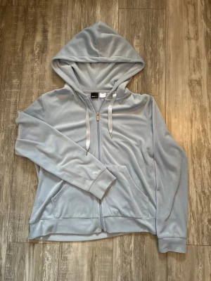 Ljus blå velour zip up kofta från Gina Tricot - Mjuk och skön ljus blå zip up hoodie i velour från Gina Tricot. Är i storlek L men passar också som en lös M, perfekt för en avslappnad och trendig look!