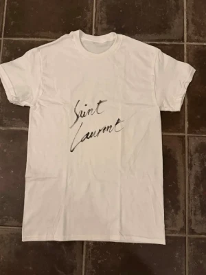 Vit t-shirt med tryck - Säljer en vit t-shirt med ett stilrent svart tryck på framsidan. T-shirten har rund hals och korta ärmar, tillverkad i ett mjukt och bekvämt material som passar perfekt till vardagslooken.