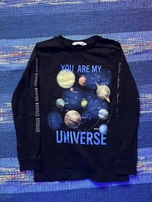 Svart långärmad topp med universumtryck - Cool svart långärmad topp med färgglatt universumtryck och texten 'You are my universe' på framsidan. Planeter och stjärnor i blått, gult och vitt. Tryck med planetnamn längs båda ärmarna. Perfekt för dig som gillar rymden och vill sticka ut.