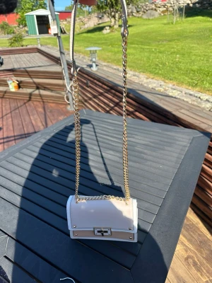 Aldo axelväska med gulddetaljer - Axelväska i beige och vit med guldfärgade metalldetaljer och kedjerem. Väskan knappt använd någonsin därav nyskick. 