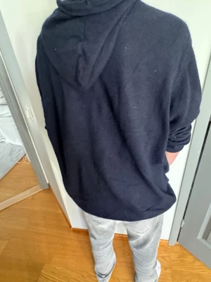 Svart hoodie i mjukt material - En stilren svart hoodie med huva och långa ärmar. Hoodien har en enkel design utan tryck eller dragkedja och är gjord i ett mjukt, bekvämt tyg som passar perfekt till jeans eller joggers.