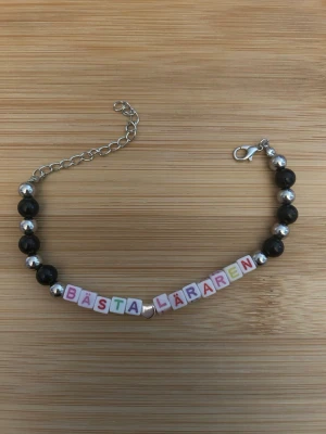 Pärlarmband med text BÄSTA LÄRAREN - Fint armband med svarta och silvriga pärlor samt färgglada bokstavspärlor som stavar 'BÄSTA LÄRAREN'. Armbandet har en silverfärgad kedja och karbinhake. Perfekt present till en lärare!