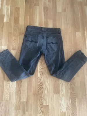 Nudie jans w27 l28 - Säljer ett par svarta jeans från Nudie Jeans med klassisk femficksdesign och svarta broderade detaljer på bakfickorna. Jeansen har normal passform och raka ben, tillverkade i mjuk bomullsdenim. Perfekta för dig som gillar stilrena och tidlösa jeans. Anledningen till försäljningen är för att dom helt enkelt inte passar längre. Modell lean Dean! W27 L28