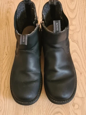 Svarta chelsea boots från Kavat - Svarta chelsea boots från Kavat i slätt läder med elastiska paneler på sidorna och dragflikar fram och bak. Grov sula och klassisk siluett som funkar till många olika stilar. Insidan är fodrad med filtmaterial för extra komfort.