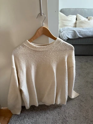 Vit stickad tröja med rund hals - Mysig vit stickad tröja med rund halsringning och långa ärmar. Tröjan har en enkel och stilren design med ribbstickade muddar vid ärmslut och nederkant. 
