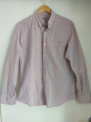 Rutig skjorta från J.Crew i bomull - Snygg rutig skjorta från J.Crew i 100% bomull. Skjortan har klassisk krage med knappar, långa ärmar och ett mönster i blått, orange och vitt. Perfekt för en stilren och avslappnad look.