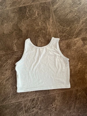 Vit croppad linnetopp - Snygg blå croppad linnetopp i enkel design. Toppen är ärmlös och har rund halsringning. Perfekt att matcha med höga jeans eller kjol för en clean look. (Plus frakt) 