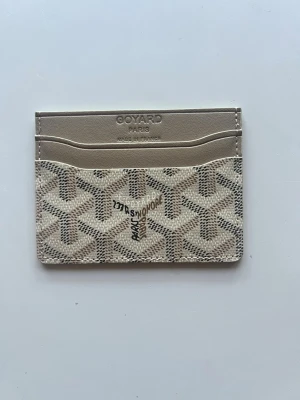 Beige kortfodral från G*yard - Snyggt och stilrent kortfodral från G*yard i beige och grått med det klassiska G*yard-mönstret. Fodralet har flera kortfack och är tillverkat i exklusivt läder med präglad logotyp på framsidan. Perfekt för dig som vill ha en lyxig accessoar i fickan.