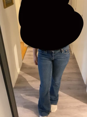 Blå bootcut jeans från Gina Tricot - Säljer ett par klassiska blå bootcut jeans från Gina Tricot. Jeansen har normal midja, fem fickor och dragkedja med knapp. De är tillverkade i denim och har en lätt utsvängd passform nertill. Perfekta för en avslappnad och trendig look.