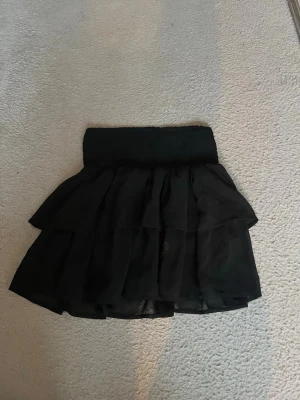 Svart volangkjol med resårmidja - Tryck gärna köp nu🩷 Snygg svart kortkjol med dubbla volanger och bred resår i midjan. Kjolen har en luftig och flowy känsla, perfekt för att styla med en crop top eller stickad tröja. Materialet känns lätt och ger kjolen ett fint fall.