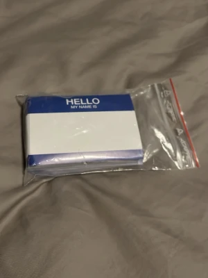 Namnskyltar med blå kant 20 stycken - Ett paket med självhäftande namnskyltar i vitt med blå kant och texten 'HELLO MY NAME IS' upptill. Perfekt för event, möten eller fester där deltagare behöver skriva sina namn. Levereras i en genomskinlig plastpåse. 20 stycken
