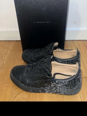 Svarta Giuseppe Zanotti  - Snygga svarta sneakers från Giuseppe Zanotti med coolt gråspräckligt mönster på hälen och sulan. Skorna har dragkedjor på sidorna, svarta skosnören och en låg profil. Insidan är ljusbeige och materialet är en mix av läder och textil.