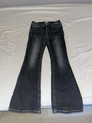 Svarta utsvängda jeans med kontrastsömmar - Säljer ett par svarta jeans med breda utsvängda ben och tydliga kontrastsömmar. Jeansen har klassisk femficksdesign och slitna detaljer framtill och baktill. Perfekta för dig som gillar retrostil och vill sticka ut med en cool siluett.