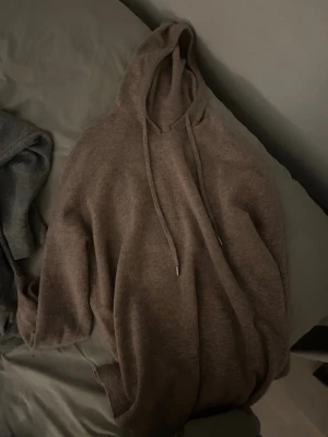 Kaschmir Hoodie - Mysig brun stickad hoodie med huva och dragsko. Tröjan har långa ärmar med ribbade muddar och är tillverkad i ett mjukt, stickat material som känns skönt mot huden. Perfekt för en avslappnad och chill stil.