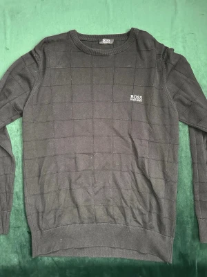 Svart tröja från Hugo Boss - Snygg svart tröja från Hugo Boss med diskret rutmönster och broderad logga på bröstet. Tröjan har rund halsringning och långa ärmar. Perfekt för dig som gillar stilrena och klassiska plagg. Pris kan diskuteras. MVH stentorparchive⚓️
