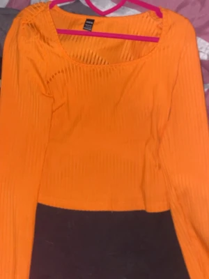 Orange ribbad långärmad topp - Trendig orange långärmad topp med ribbad struktur och rundad urringning. Snygg croppad passform som passar perfekt till jeans eller kjol. Materialet känns mjukt och stretchigt, vilket gör den bekväm att bära hela dagen.