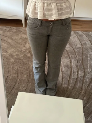 Grå bootcut-byxor med lågmidja från Zalando - Snygga grå bootcut-byxor från zalando med klassisk femficksdesign och hällor för skärp. Byxorna har en lätt utsvängd passform och stängs med dragkedja och knapp. Perfekta för en trendig och avslappnad look.