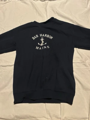 Marinblå sweatshirt Bar Harbor Maine - Mysig marinblå sweatshirt med tryck 'Bar Harbor Maine' och ett ankare på bröstet. Klassisk rund halsringning och långa ärmar. Perfekt för en avslappnad look och enkel att matcha med jeans eller shorts.