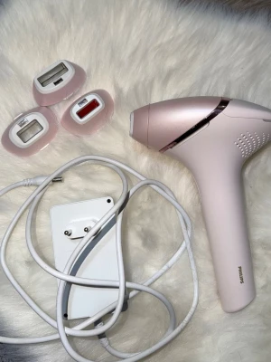 Philips Lumea IPL hårborttagningsapparat - Säljer en Philips Lumea IPL hårborttagningsapparat i ljusrosa i bra skick med fyra olika utbytbara munstycken för kroppen och ansiktet, samt en medföljande vit strömadapter. Ergonomisk design i plast med metallic-detaljer. Perfekt för smidig hårborttagning hemma.