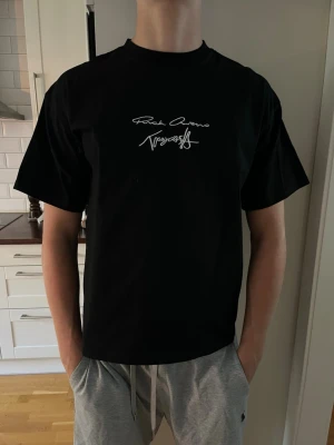 Svart Rick Owens x Tommy Cash t-shirt - Säljer en svart t-shirt från Rick Owens i samarbete med Tommy Cash. T-shirten har vit grafisk text framtill och stora tryck i vitt på ryggen. Oversized passform och klassisk rund hals. Perfekt för dig som gillar streetwear och unika samarbeten.