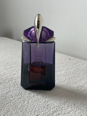 Mugler Alien Eau de Parfum 60ml - Alien från Mugler är en ikonisk parfym i en lila, geometrisk glasflaska med silverfärgad detalj på toppen. Flaskan har en futuristisk och lyxig känsla, perfekt för dig som gillar unika dofter och snygg design på parfymhyllan.