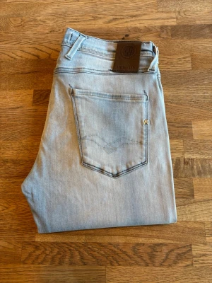 Ljusblåa jeans från replay - Säljer ett par ljusblåa jeans från replay med klassisk femficksmodell och en liten slitning på ena benet. Jeansen har raka ben och är tillverkade i mjuk denim. Perfekta för en avslappnad och trendig look.