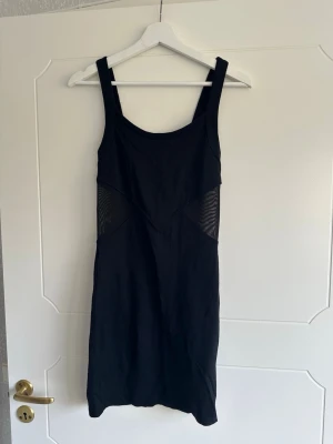 Klänning - Kortare klänning med meshdetaljer i sidan. Dragkedja och knäppning i ryggen. Glansigt tyg på insidan. En tråd som gått upp annars okej skick.