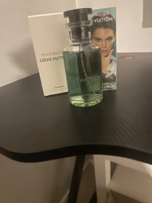 Louis Vuitton Imagination parfym 100ml - Lyxig parfym från Louis Vuitton, Imagination, i en elegant glasflaska med svart lock. Parfymen har en fräsch grön nyans och kommer i originalförpackning. Flaskan rymmer 100 ml Eau de Parfum och har en modern, stilren design.