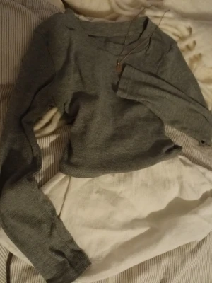 Grå långärmad tröja med rund hals - En enkel och stilren grå långärmad tröja med rund halsringning. Tröjan är i mjukt, stickat material och har en klassisk passform som passar perfekt till jeans eller kjol. Perfekt för lager-på-lager-stil under kyligare dagar. ENDAST den gråa toppen, inte de vita toppen under. Vita toppen är endast där för att visa hur man kan lagra den.