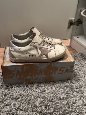 Vit/silviriga Golden Goose skor - Säljer ett par sjukt feta Golden Goose skor i fint skick. Dom har används lite men inget som hindrar dig. Allt i bilderna medföljer🤗 kom med prisförslag✨ och vill du har med info är det bara att lämna ett meddelande💕Det är storlek 40 och sulan är 26 cm lång. Passar även 40 1/2 eller 41✨ jag har 41 och dom passar.