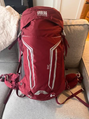 Vinröd Urberg 55L ryggsäck - Säljer en vinröd Urberg ryggsäck på 55 liter med vita och grå detaljer. Ryggsäcken har flera justerbara remmar, vadderade axelband och höftbälte med fickor. Perfekt för längre äventyr och har smarta fack för packning. Materialet är slitstark syntet.