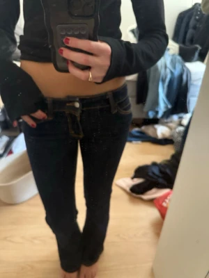 Mörkblå bootcut jeans med låg midja - Säljer ett par mörkblå bootcut jeans med låg midja och klassiska fickor. Jeansen har kontrastsömmar och en snygg passform som framhäver benen. Perfekta för en trendig och avslappnad look. STORLEK 27/32!