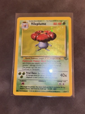 Vileplume Pokémonkort Base Set - Säljer ett Vileplume holografiskt samlarkort från Pokémon Base Set, nummer 15/64. Kortet har gul ram, glittrig bakgrund och motiv av Vileplume med röda blommor. Perfekt för dig som samlar Pokémonkort eller gillar retroprylar.