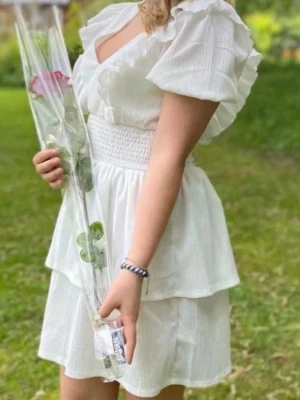 Vit volangklänning med v-ringning - Superfin vit kortklänning från Gina tricot med v-ringning, volangdetaljer och puffärmar. Klänningen har smock i midjan och dubbla lager i kjolen för en extra flowy känsla. Perfekt för sommarens alla tillfällen.