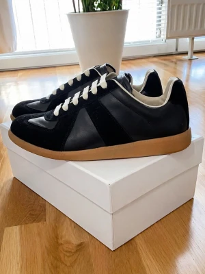 Maison Margiela Skor - Stilrena svarta sneakers från Maison Margiela med beige sula och vita skosnören.  