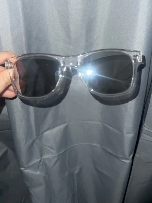 Transparenta solglasögon med svarta glas - Snygga solglasögon med transparent båge och svarta glas från hammarby shopen.Klassisk fyrkantig form som passar till de flesta stilar. Märkta med Stadium-logga på sidan. Perfekta för soliga dagar och en cool look. Aldrig använda. Påse medföljer. Kan sänka priset vid snabb affär