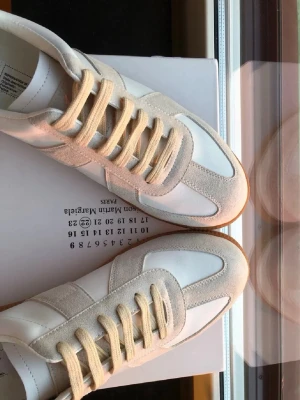 Maison Margiela gats  - Snygga Maison Margiela gats i vitt och beige med ovandel i mocka och läder. Klassisk gummisula och beigea skosnören. Perfekt för dig som gillar stilrena och tidlösa sneakers med premiumkänsla.