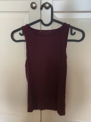 Vinröd ärmlös linnetopp -  en enkel vinröd linnetopp med rund halsringning. Toppen är ärmlös. Materialet känns mjukt och stretchigt. Vet inte exakt storleken då lappen är borta men tror den är från lager 157 storlek M. På längden är den 19-20 cm