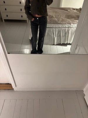 Svarta raka jeans med låg midja - Säljer ett par svarta jeans med rak passform och låg midja. Jeansen har klassisk femficksdesign och knappgylf. Perfekta för en avslappnad och trendig look. Materialet ser ut att vara denim i bomull.