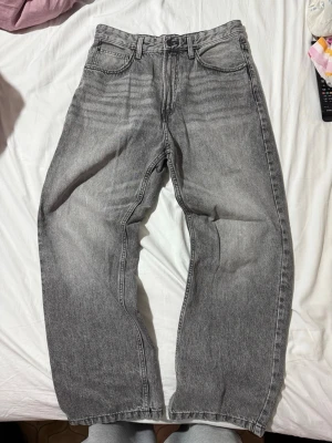 Gråa raka jeans med vintagekänsla - Säljer ett par gråa jeans med rak passform och klassisk femficksdesign. Jeansen har en tvättad vintage-look och är tillverkade i kraftig denim. Perfekta för dig som gillar en avslappnad och tidlös stil.