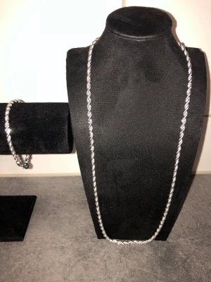 Silverfärgat tvinnat halsband - Säljer ett stilrent halsband i silverfärg med tvinnad kedja. Halsbandet har en enkel men snygg design som passar till många olika looks. Materialet ser ut att vara metall och kedjan har en glansig finish. Perfekt för dig som gillar minimalistiska accessoarer.