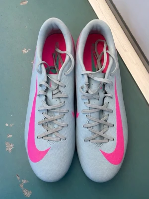 Nike ljusblå fotbollsskor med rosa swoosh - Använde de några gånger men de va för tajta för min fot och därför ska jag sälja de. Det finns inga fel me skorna, skriv bara om ni undrar något