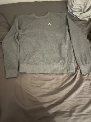 Grå crewneck från Jordan - Snygg grå crewneck från Jordan med klassisk Jumpman-logga broderad på bröstet. Tröjan har rund hals, långa ärmar och ribbade muddar vid ärmslut och nederkant. Perfekt för en avslappnad och sportig stil.