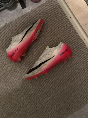 Nike Mercurial fotbollsskor röd/vit - Säljer ett par Nike Mercurial fotbollsskor med snygg design i vitt och rött, samt svart swoosh längs sidan. Skorna har låg profil och är tillverkade i syntetmaterial för bästa känsla och grepp på planen. Perfekta för dig som vill ha snabbhet och stil på fotbollsplanen.