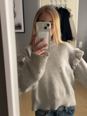 Grå stickad tröja med volang  - Säljer en ljus grå stickad tröja med volang vid axlarna. Super fin om man vill ha en basic look. Tröjan är i storlek 158/164 men passar som Xs. 😊